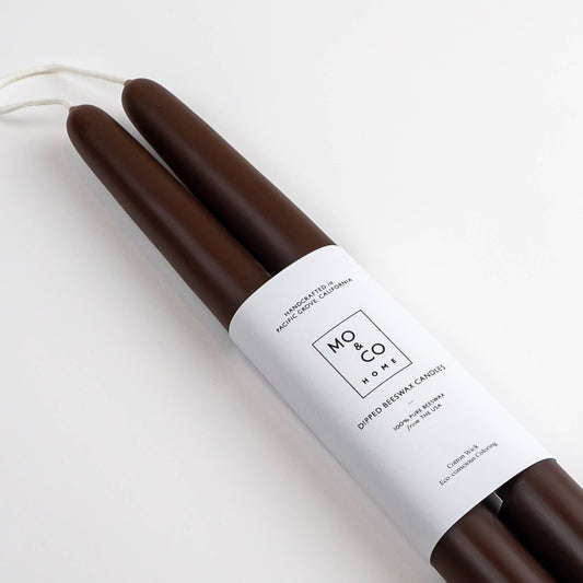 Two brown beeswax taper candles with a white label on a light gray background
