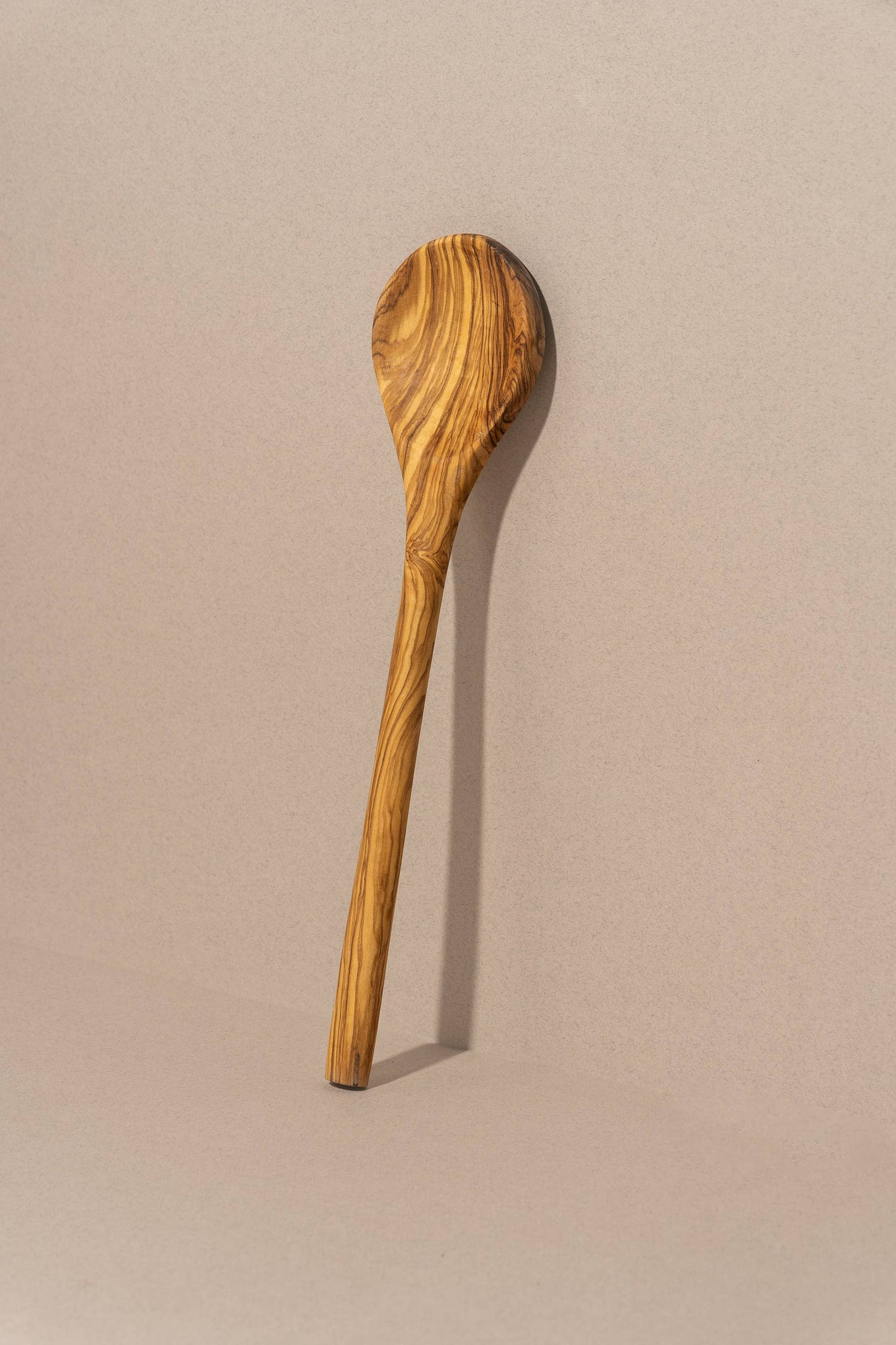 A single olive wood cooking spoon with a smooth finish and a handle, placed against a neutral background.
