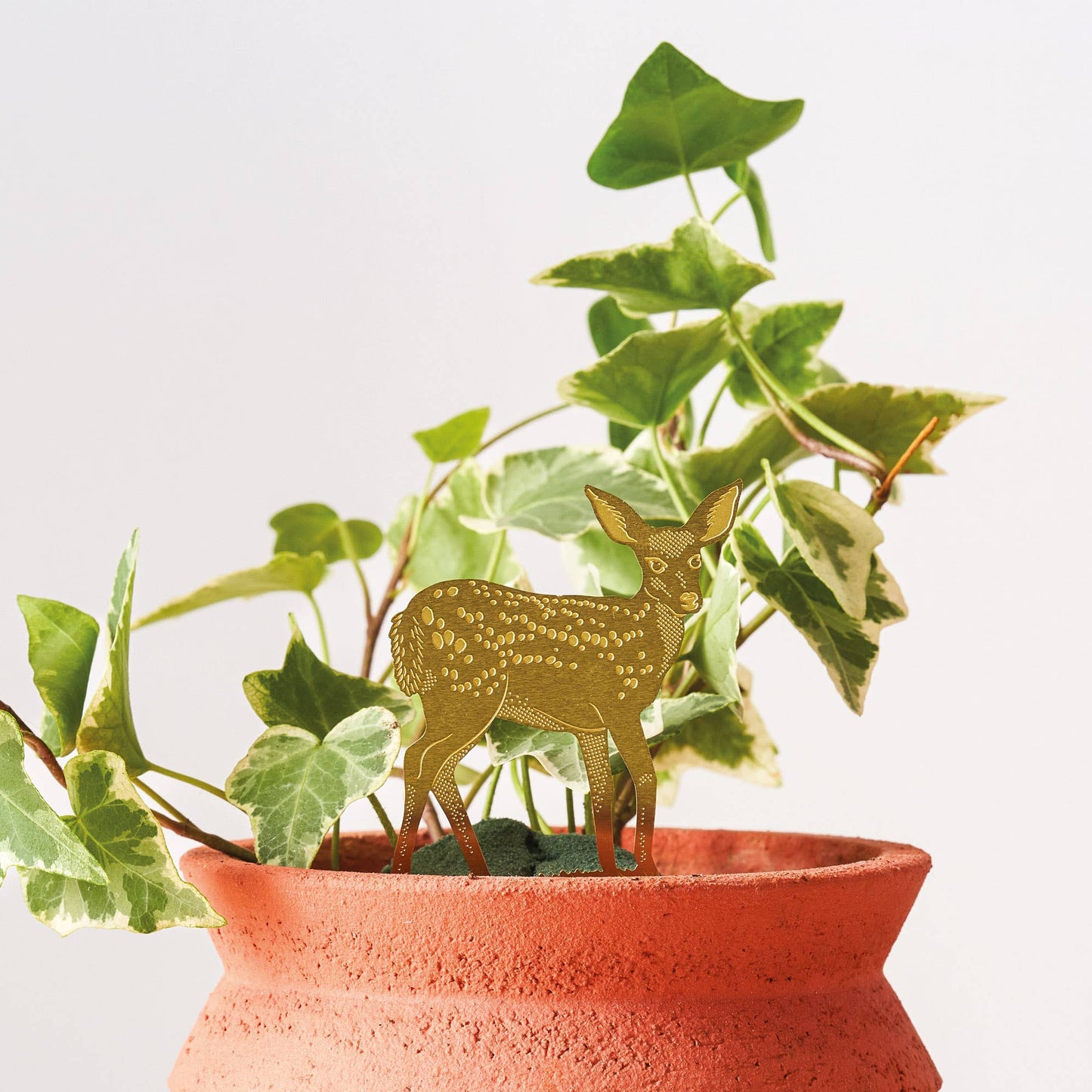 A brass deer figurine placed inside a potted plant, with green leaves surrounding it.