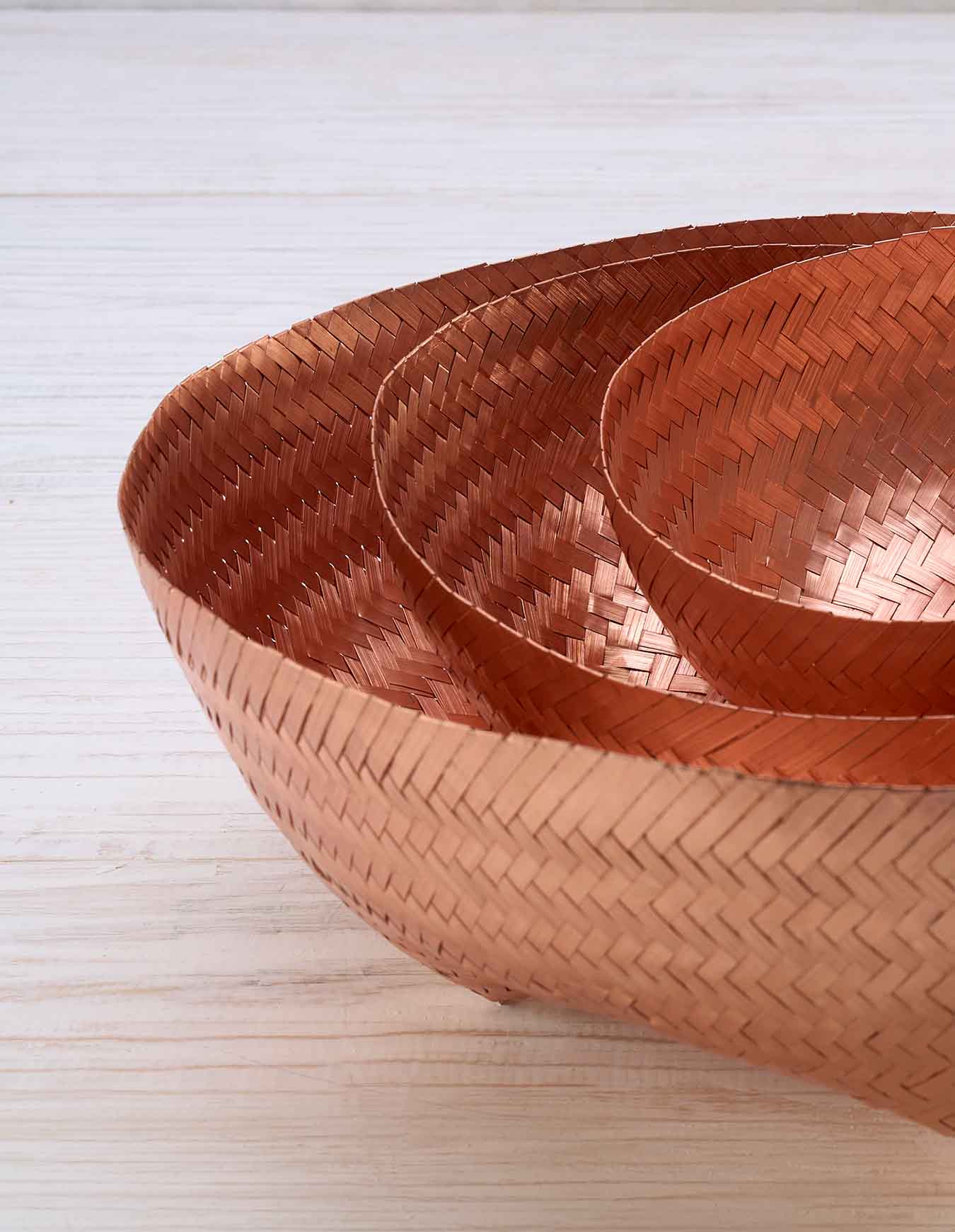 A close-up shot of three copper woven bowls sitting nested within each other on a white surface