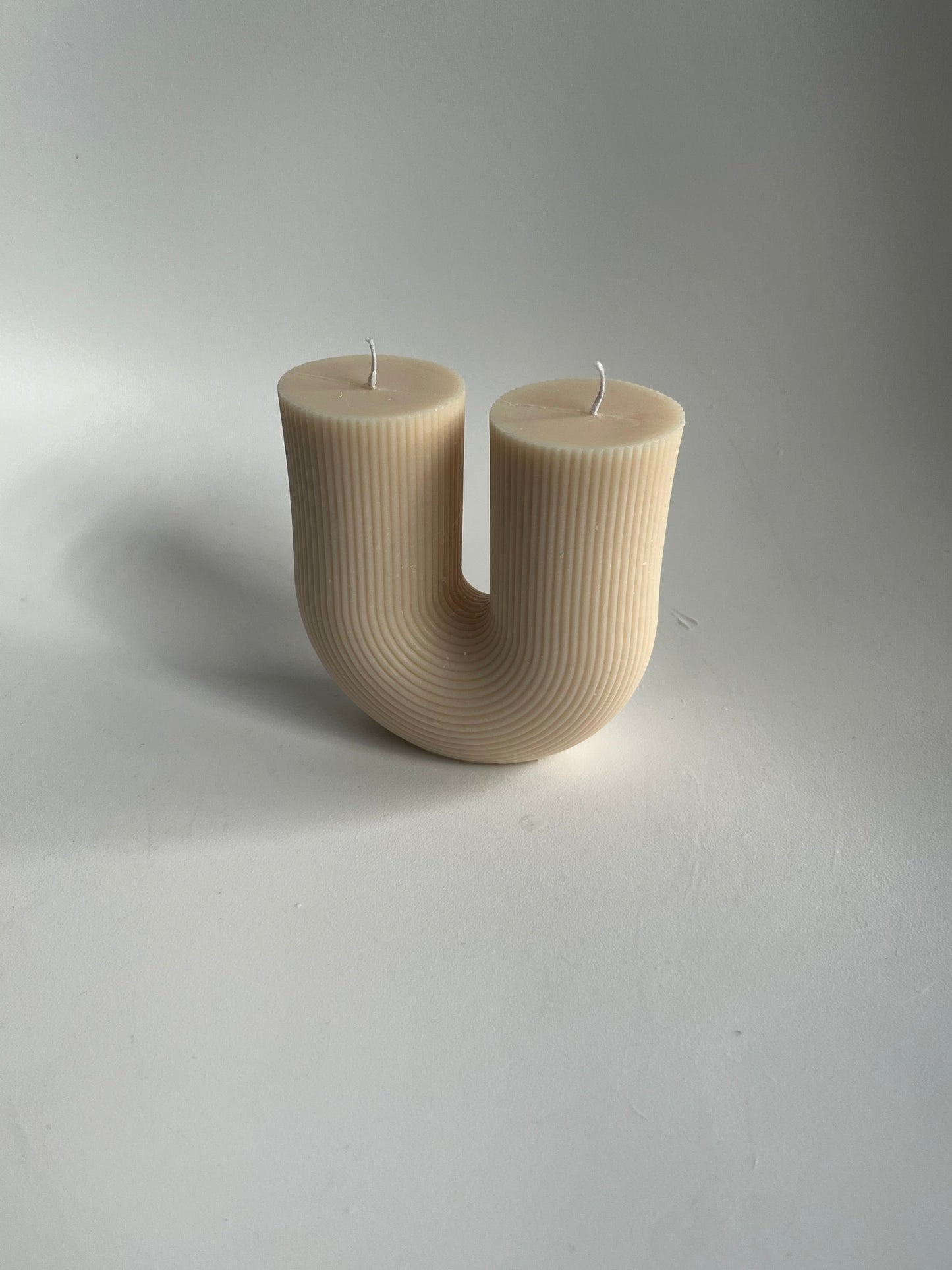 A top-down angled view of a u-shaped wax candle with ribbed detailing with a pale gray background