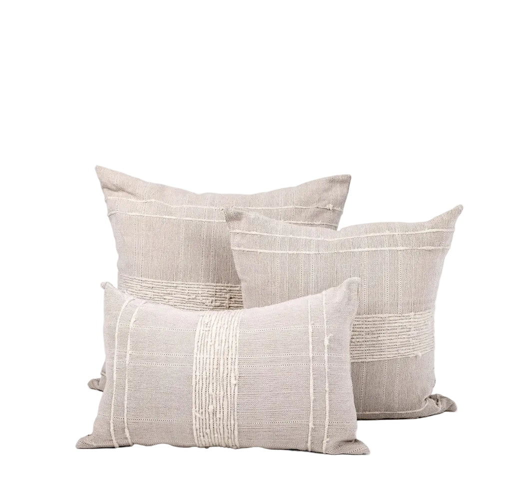 Trio of multi-sized square and rectangular pillows with sand-colored wool and cotton covers featuring woven ivory striping details sits against white background