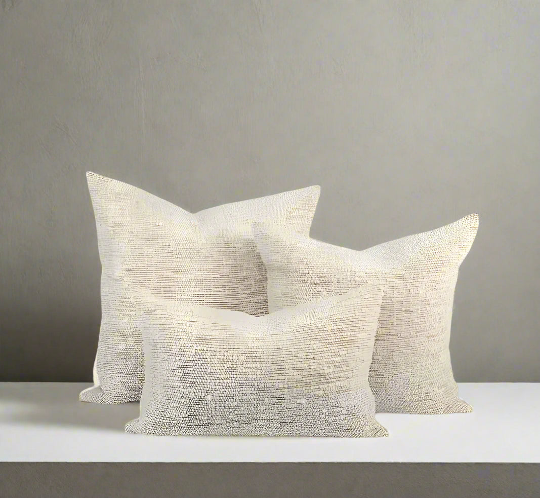 A trio of multi-sized sand- and ivory-colored nubby wool pillows sits against a white background