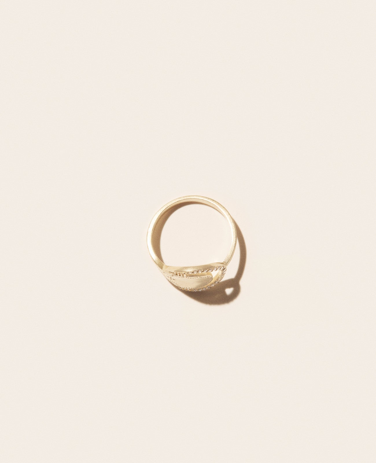 A gold ring with a round shape tucked into a half-ring of diamonds set against an off-white background shown from the side view