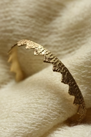 Gold crown-like cuff bracelet on a textured beige surface