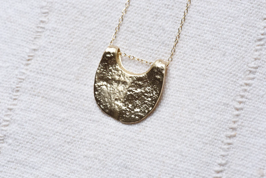 Gold necklace with a half-moon pendant on an off-white textured background