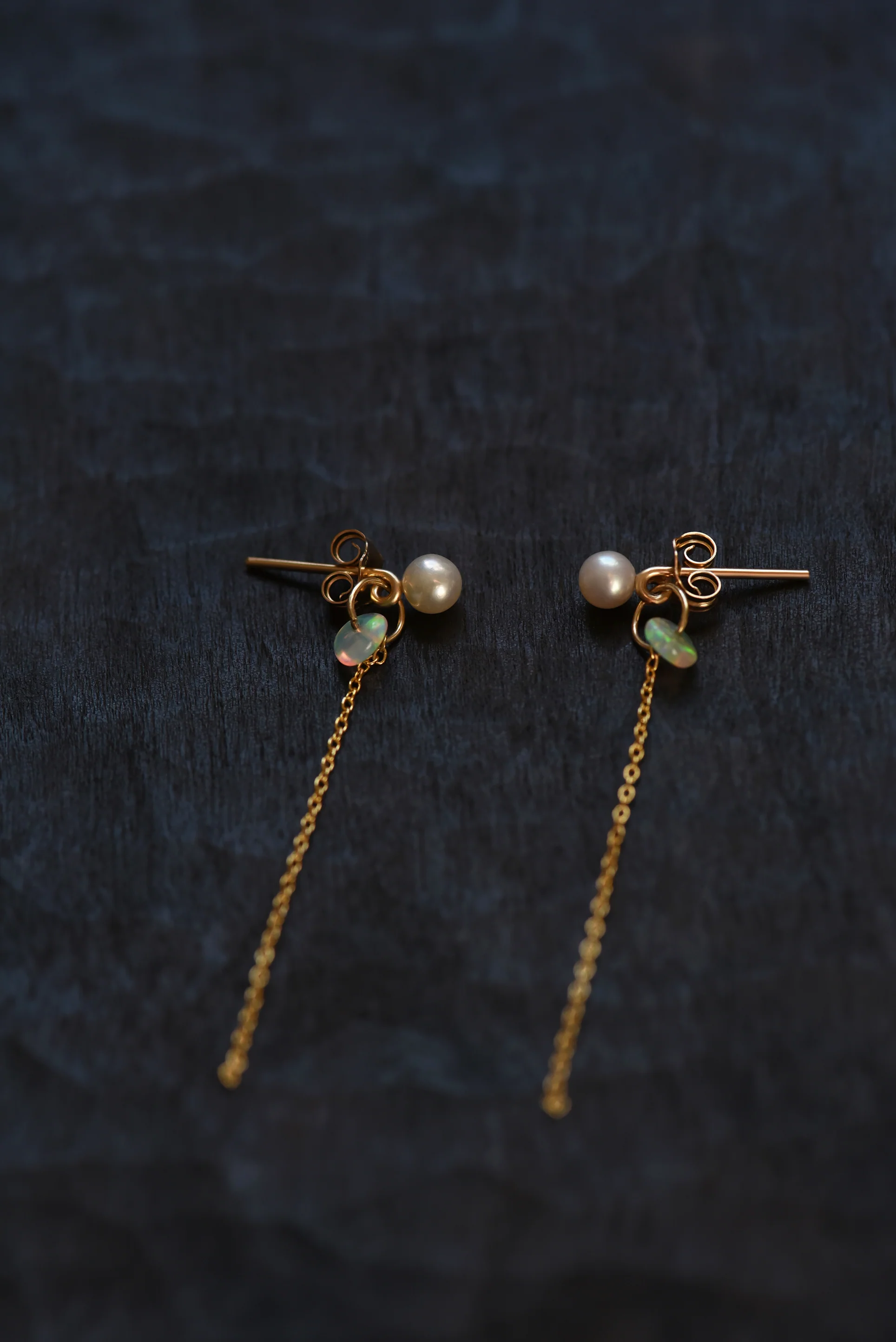 Pair of gold chain earrings with pearl and opal accent on a dark gray suede background