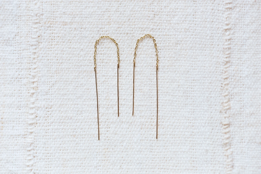 Two gold threader earrings on a textured white cloth background
