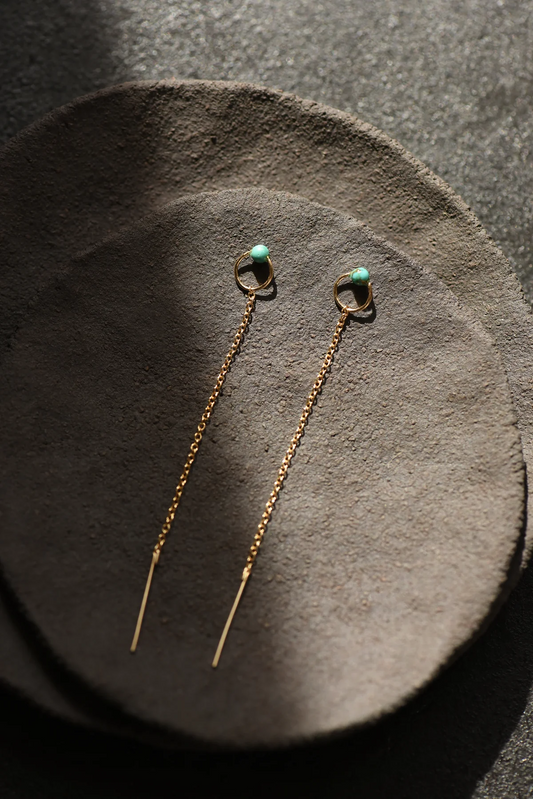 Pair of gold threader earrings with turquoise accent on a gray suede surface