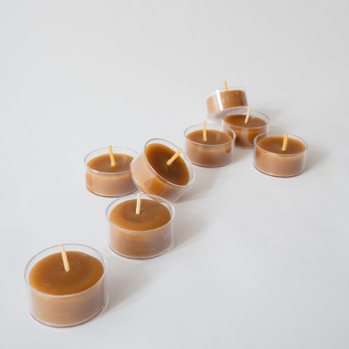 A group of hand-poured beeswax tea light candles arranged on a white surface, with a warm brown color and unlit state.