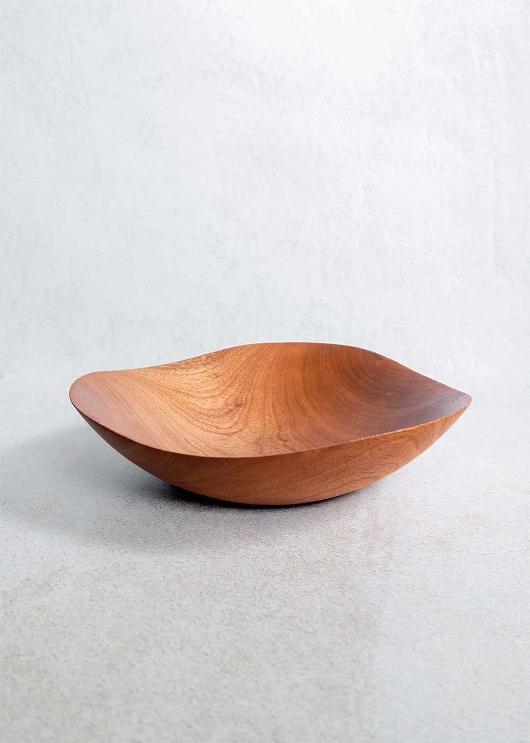 A handcrafted mahogany wood bowl with a curved shape, displayed on a textured surface.