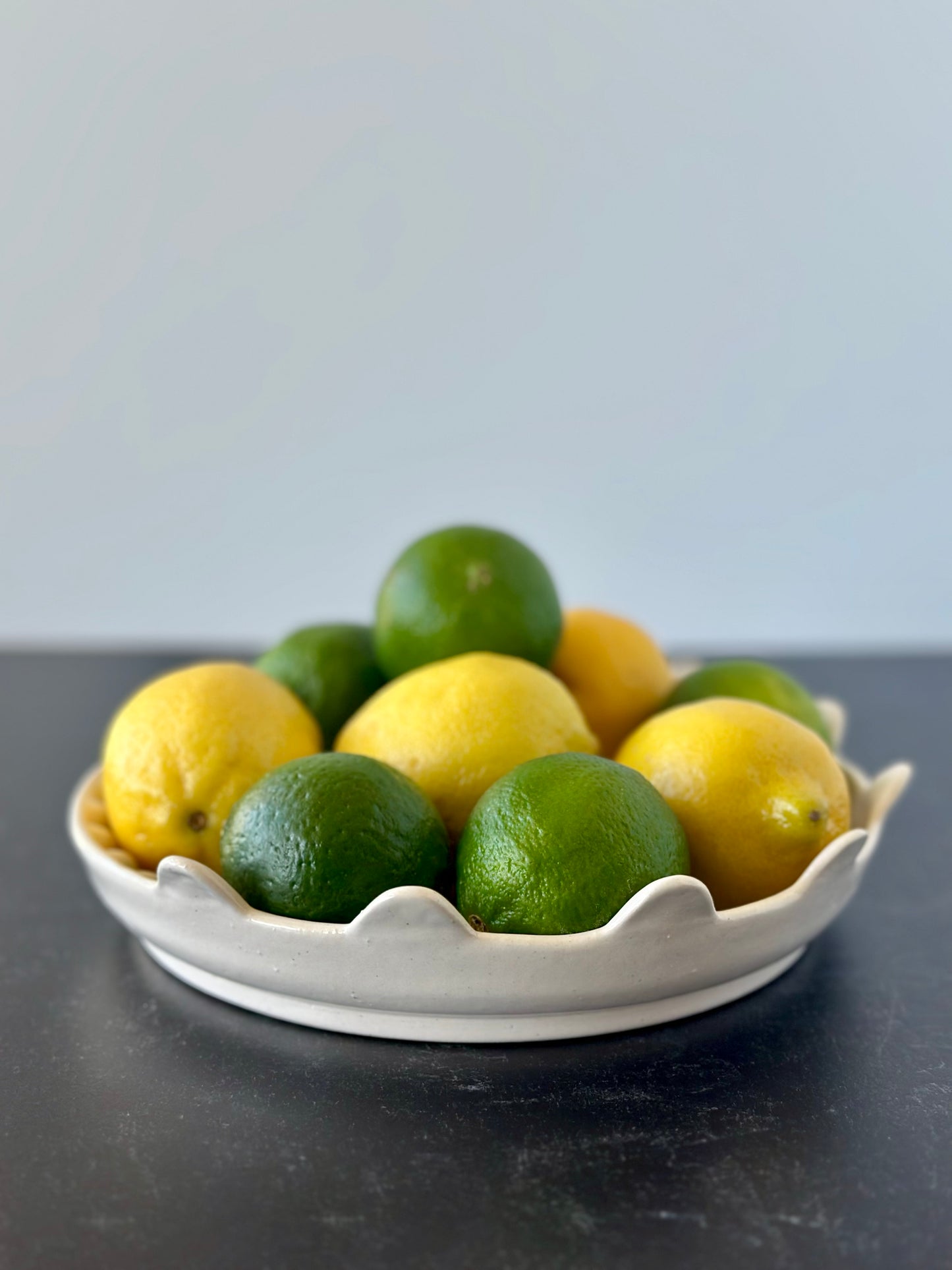 A handcrafted ceramic plate with a feather pattern, displaying lemons and limes on a dark surface.