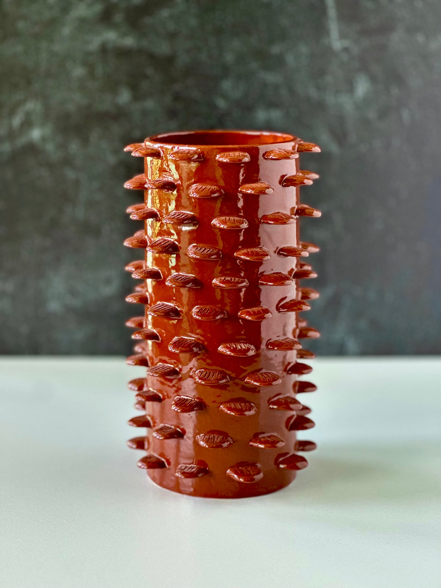 A conical ceramic vase with a cinnamon color and decorative details resembling feathers or the texture of a palm tree trunk
