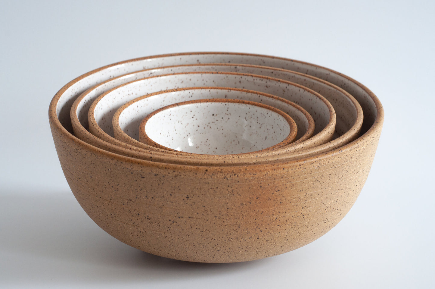 A set of five white ceramic nesting bowls with a speckled pattern, displayed in descending size order with the smallest on the top and the largest at the bottom.