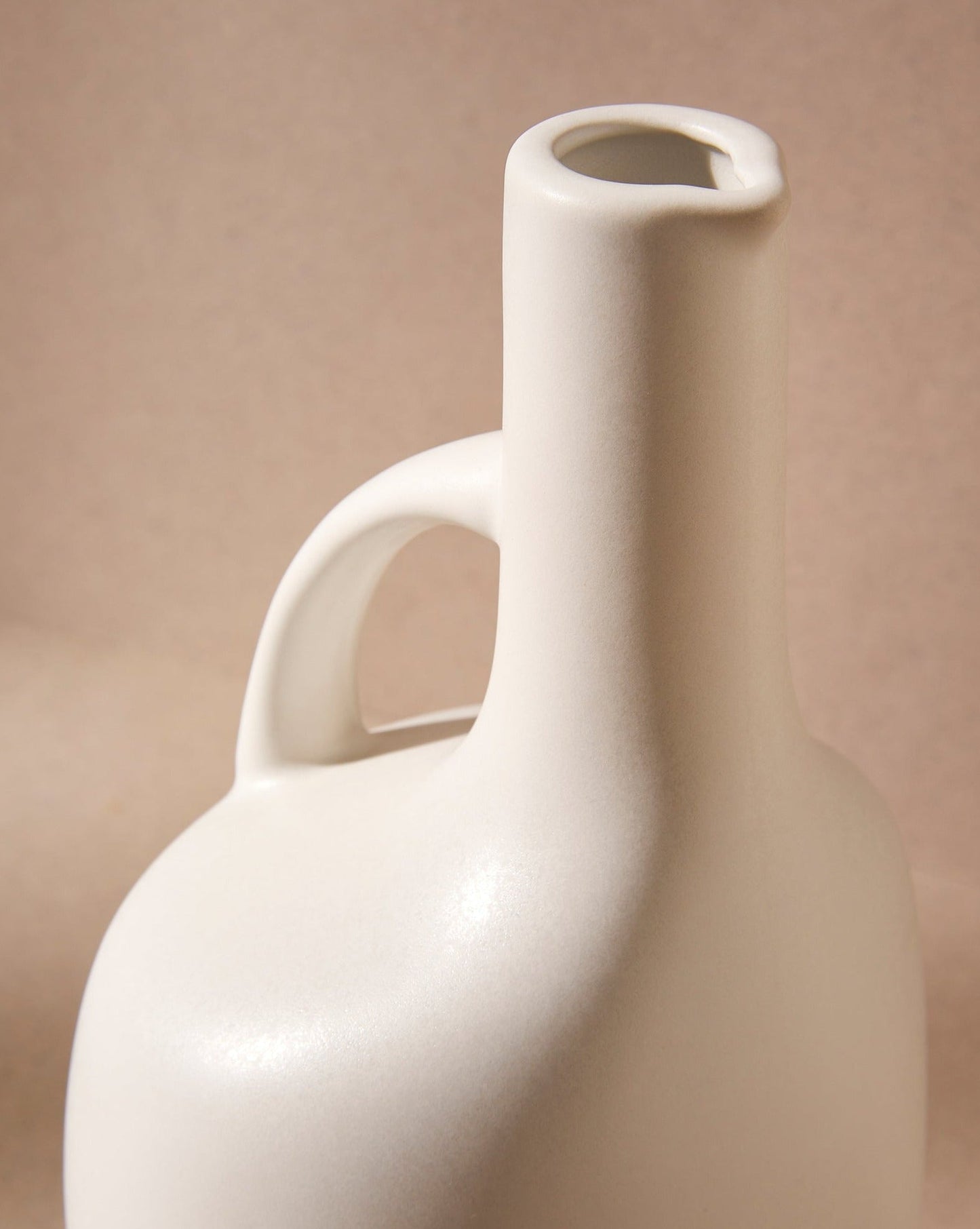 A close up of the upper portion of a white ceramic olive oil dispenser with a handle featuring the spout feature of the opening