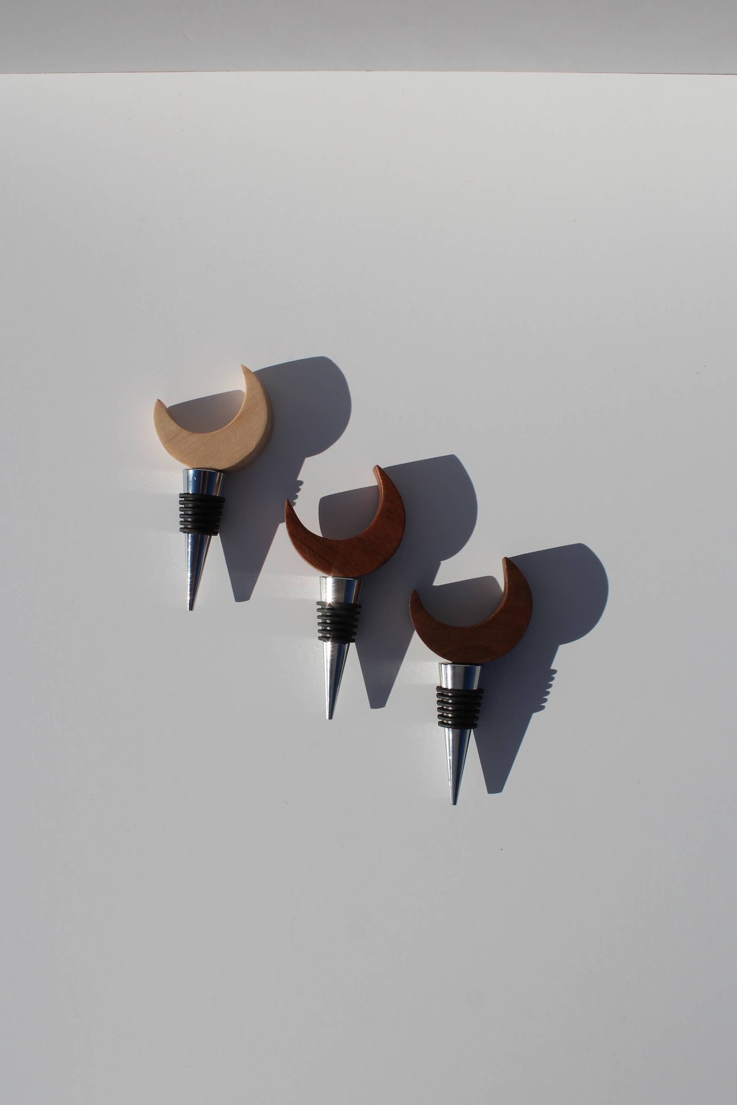 Three wooden wine bottle stoppers with crescent moon designs on a light gray background