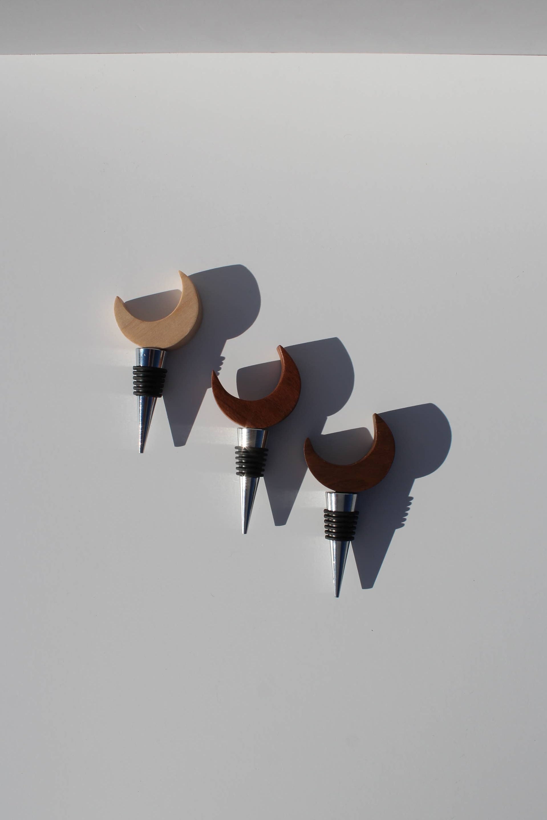 Three wooden wine bottle stoppers with crescent moon designs on a light gray background