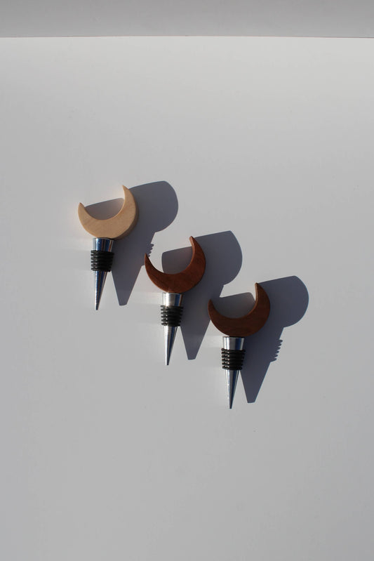 Three wooden wine bottle stoppers with crescent moon designs on a light gray background