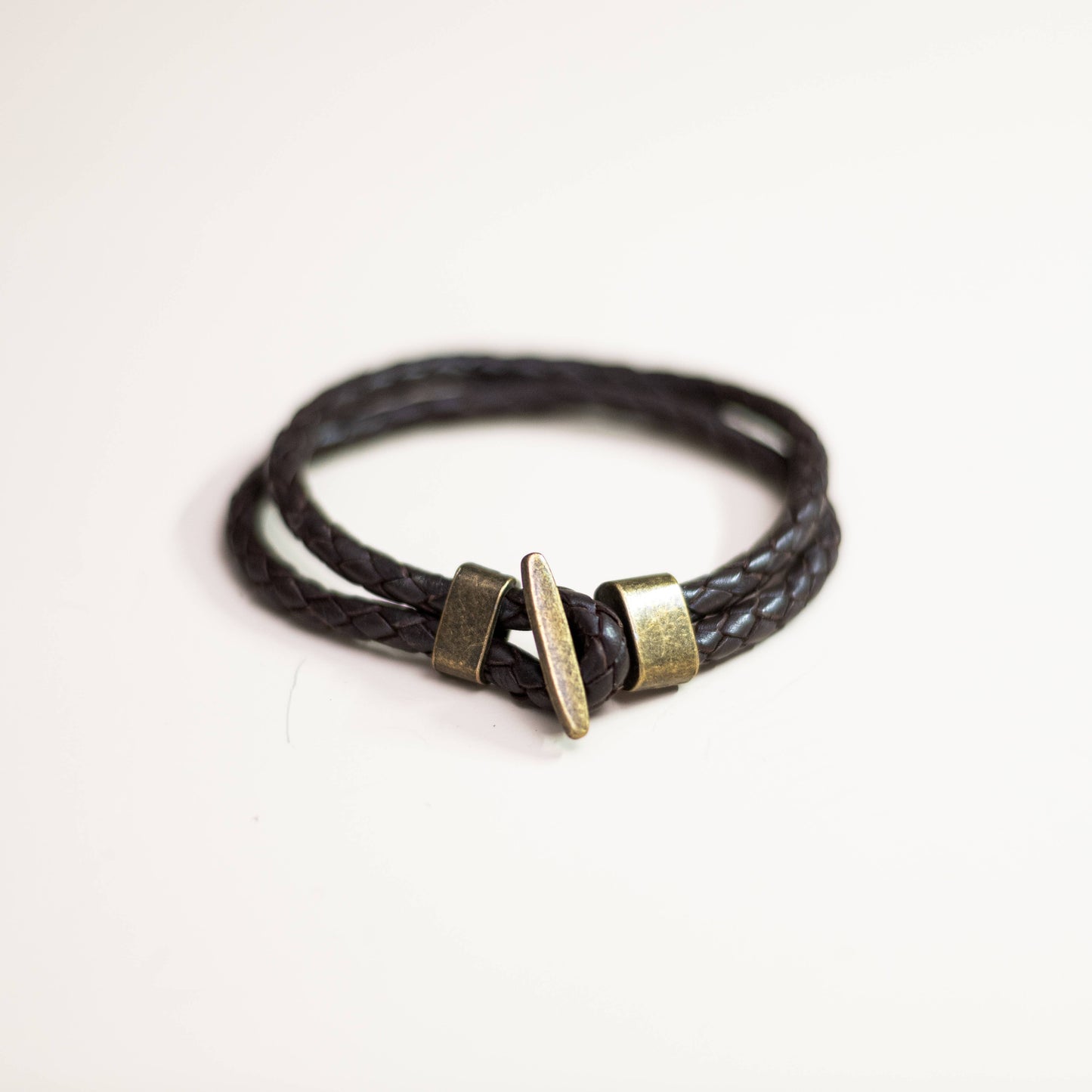 Black braided leather bracelet with brass accents on a soft white background