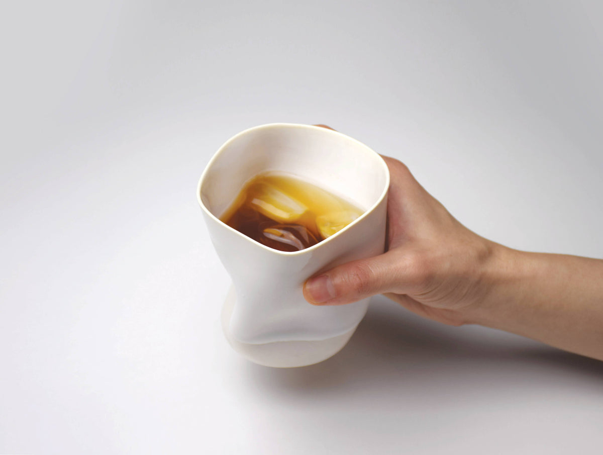 Hand holding a white ceramic cup with whiskey on a light gray background