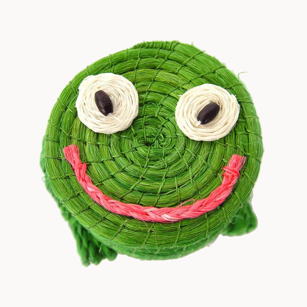 Green woven lidded basket with a face of a frog stitched on the top and set against a white background