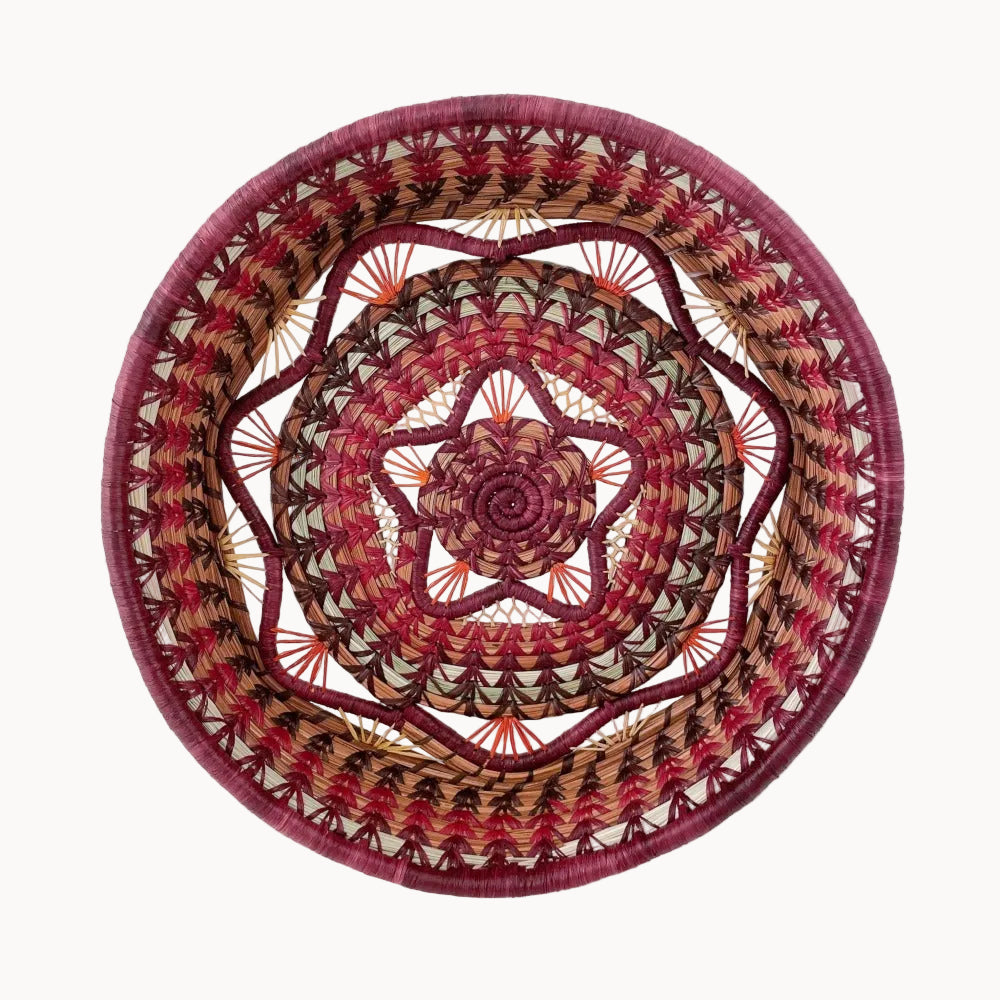 Woven basket in shades of red, burgundy, beige and pale green with a concentric circular pattern on a white background