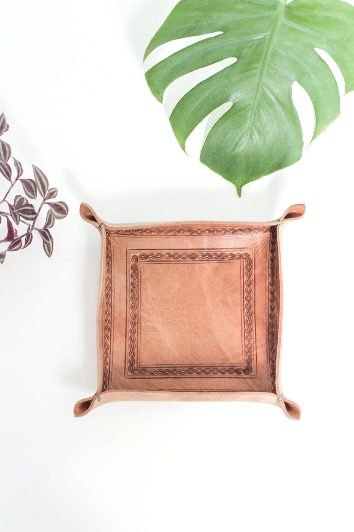 Natural leather tray on a white surface with green leaves in the background