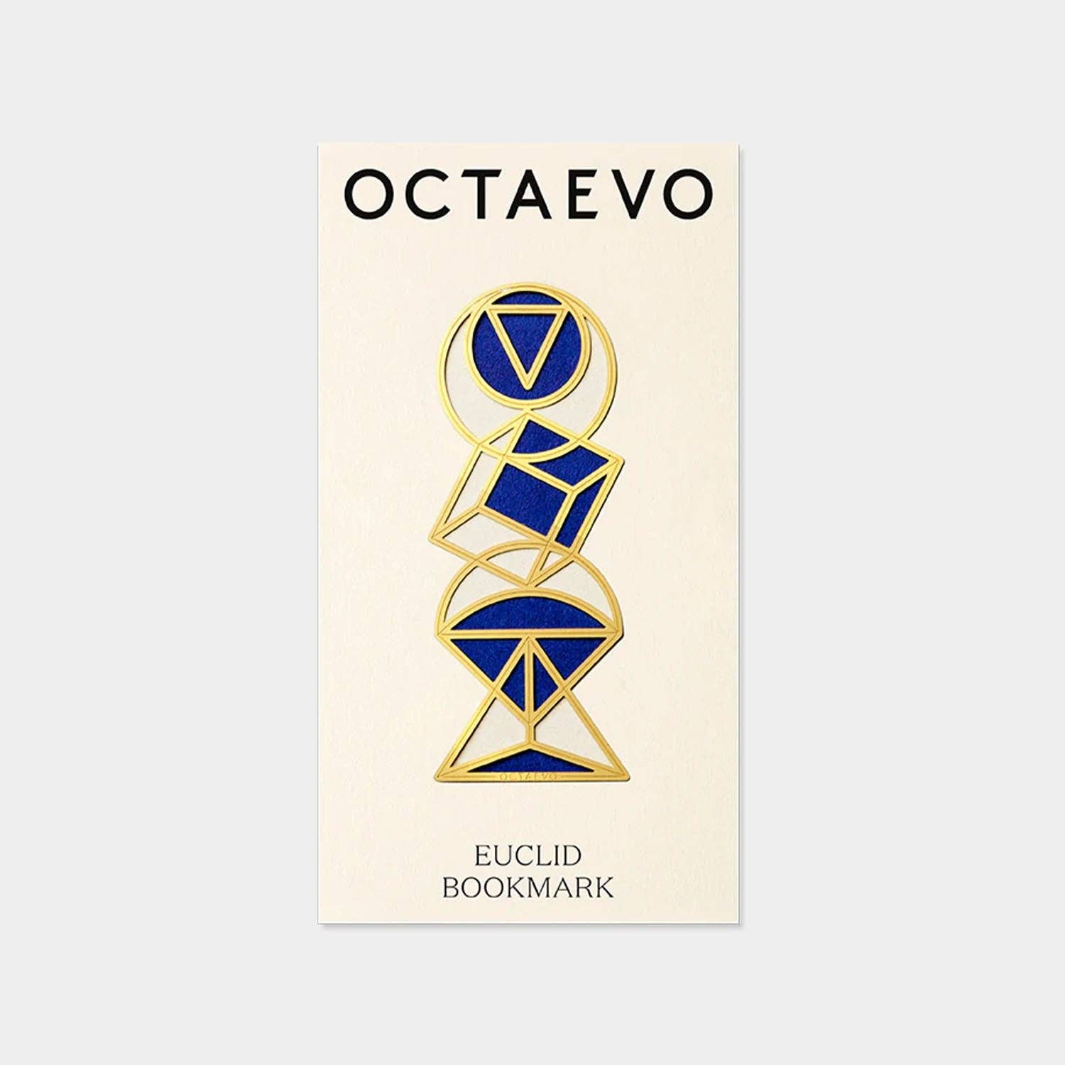 A brass bookmark with a geometric design, featuring a triangle and a circle, presented on a post-card sized mount with the text 'OCIAEURO' and 'EUCLID BOOKMARK'.