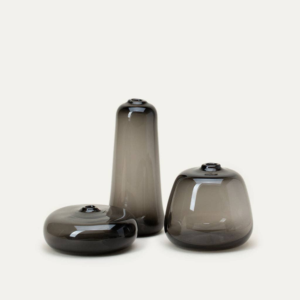 Three smoky grey glass vases of different sizes on a light beige background
