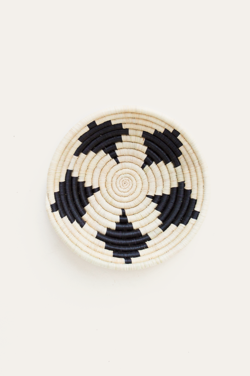 Round woven basket with black and white pattern on a beige background