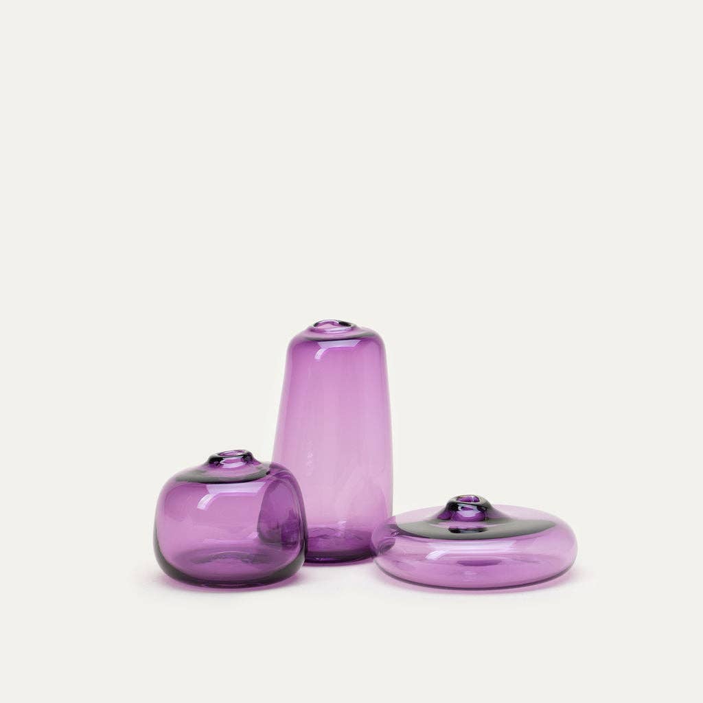 Three purple glass vases of different shapes on a white background
