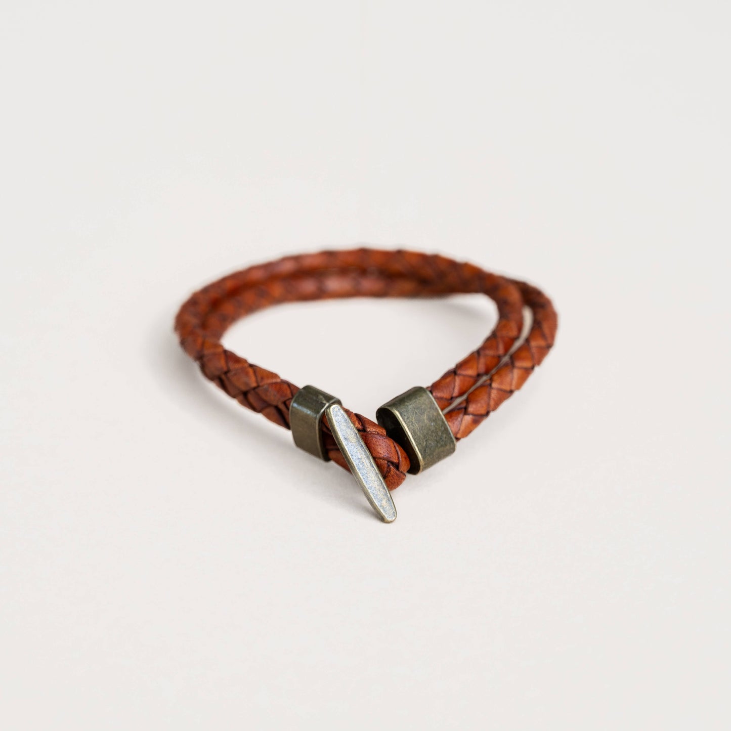 Tan braided leather bracelet with metal clasp on a soft white background