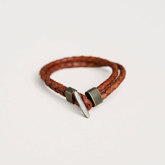Tan braided leather bracelet with metal clasp on a soft white background