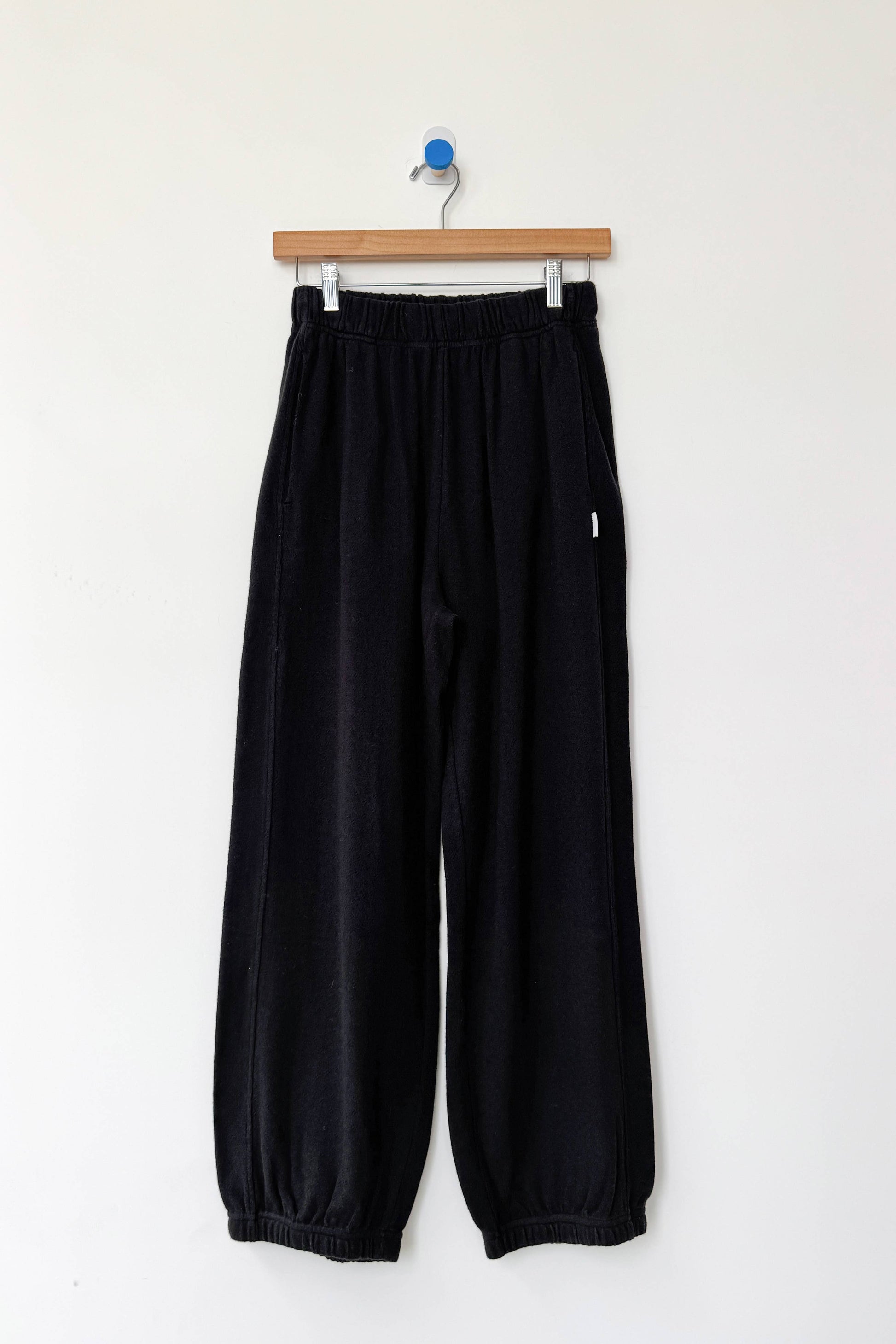 Black pants hanging on a wooden hanger against a white background