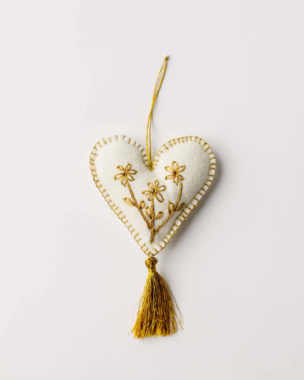 Heart-shaped ornament with floral embroidery and a tassel on a light background
