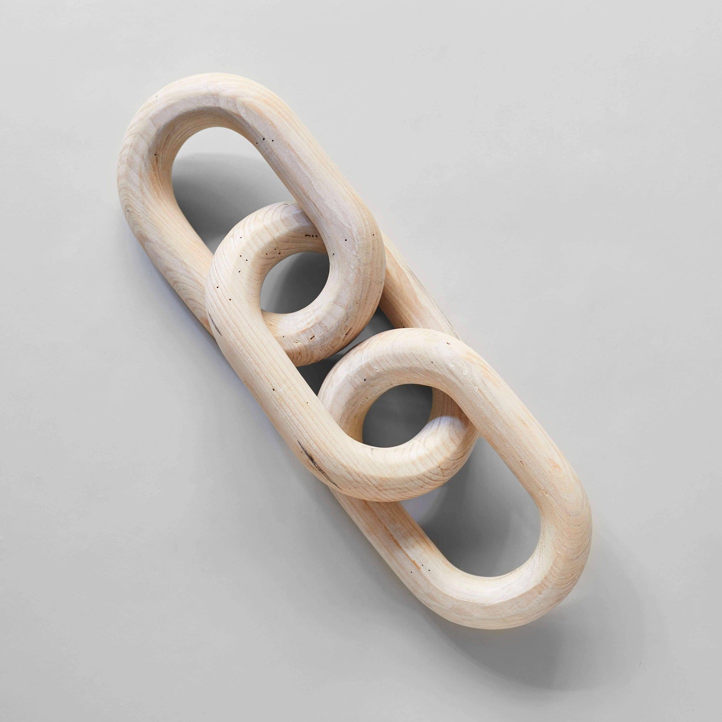 A wooden chain link with three rings sitting on a pale gray surface