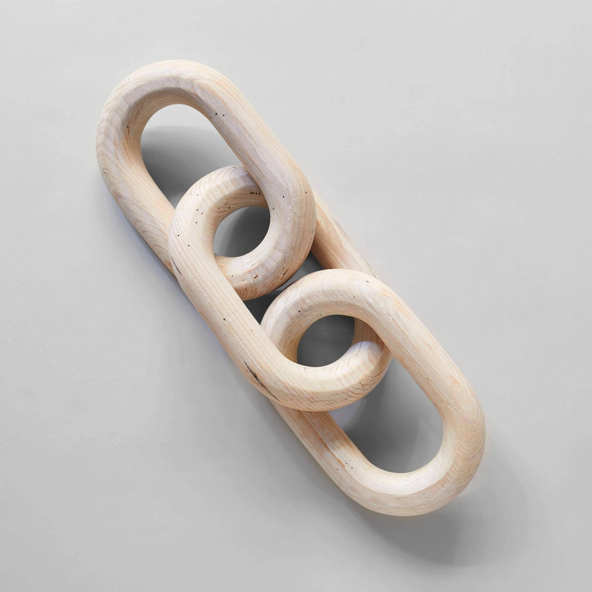 A wooden chain link with three rings sitting on a pale gray surface
