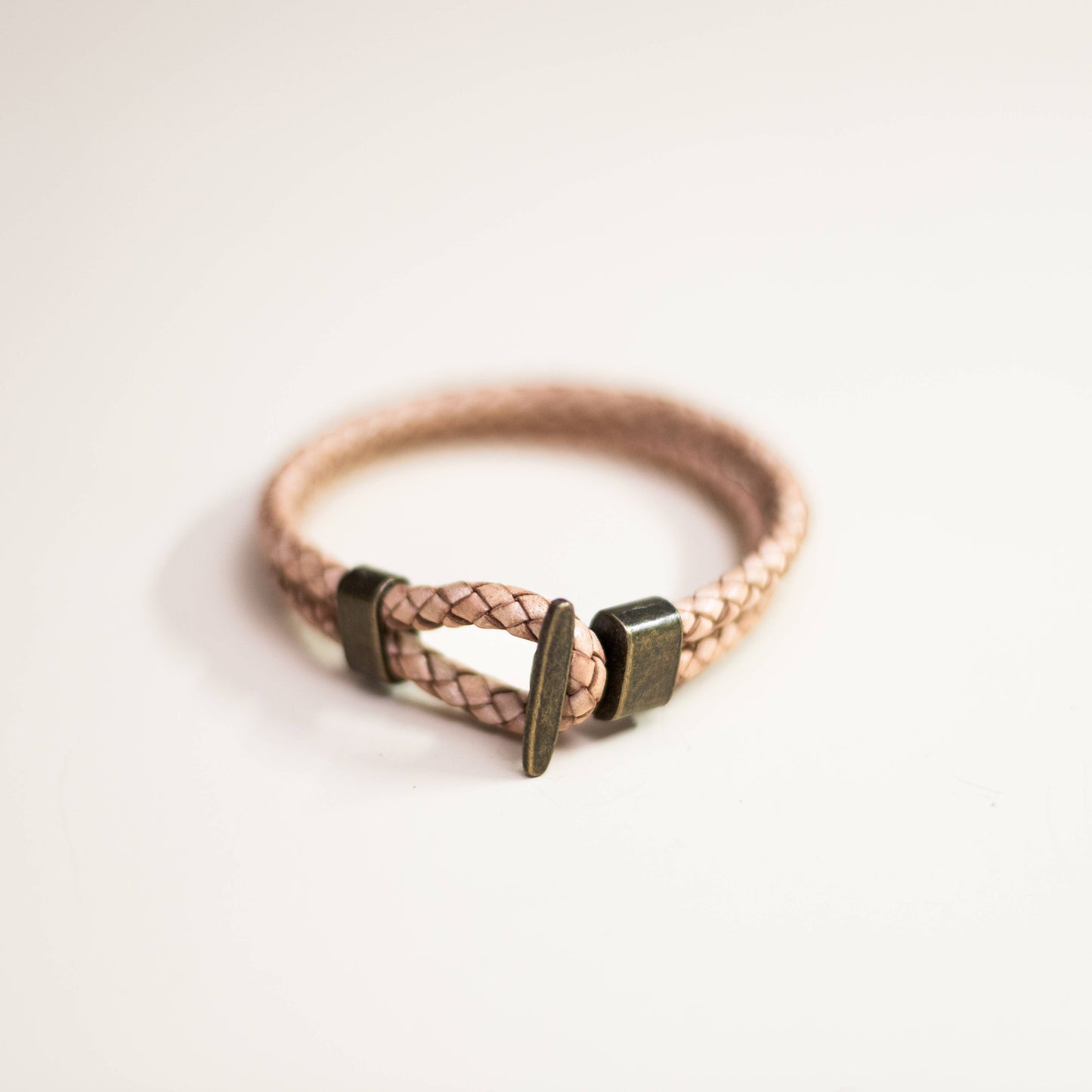 Natural colored leather braided bracelet with bronze clasp on a light background
