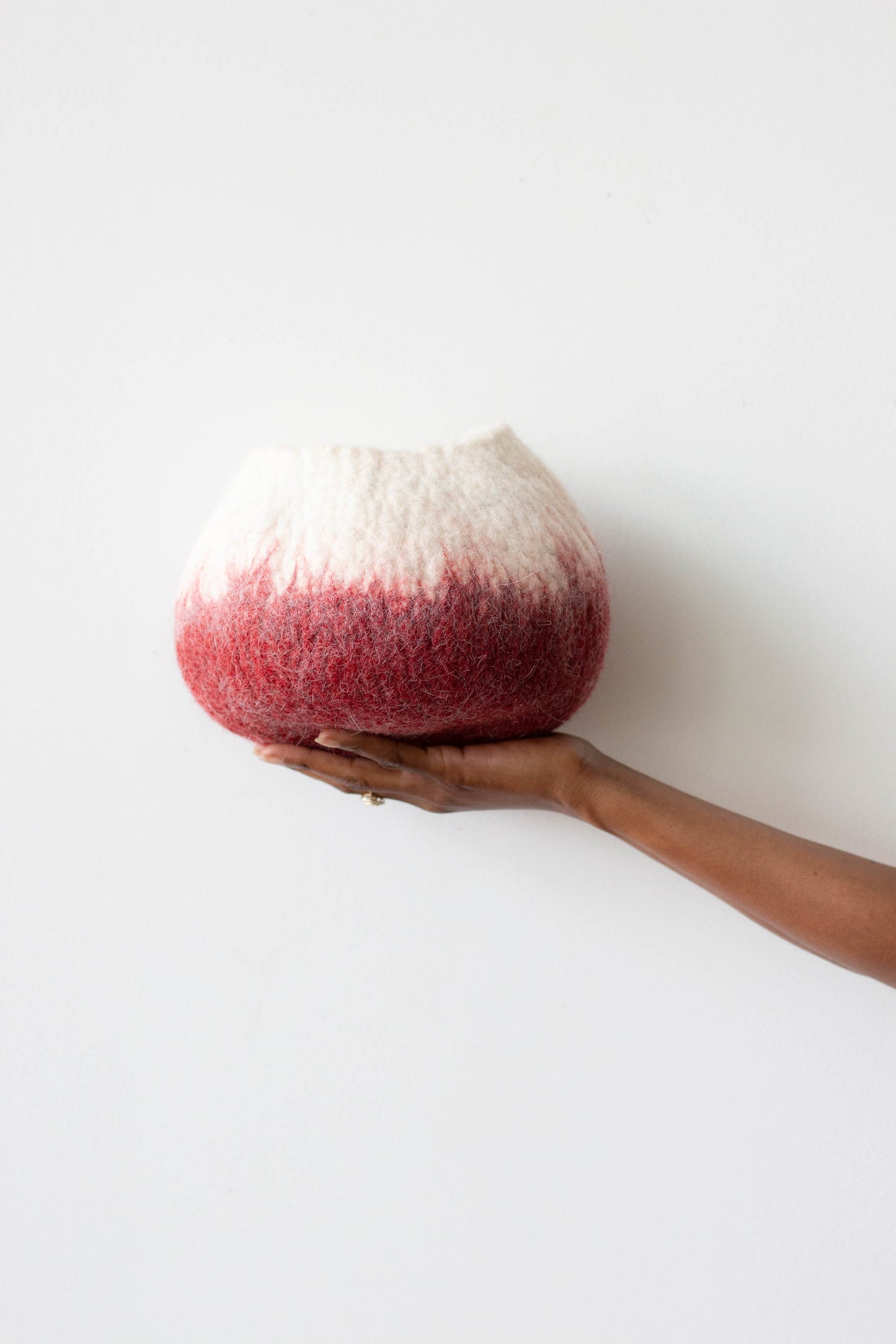 Woman's hand holding white and deep red ombre wool decorative basket against a white background