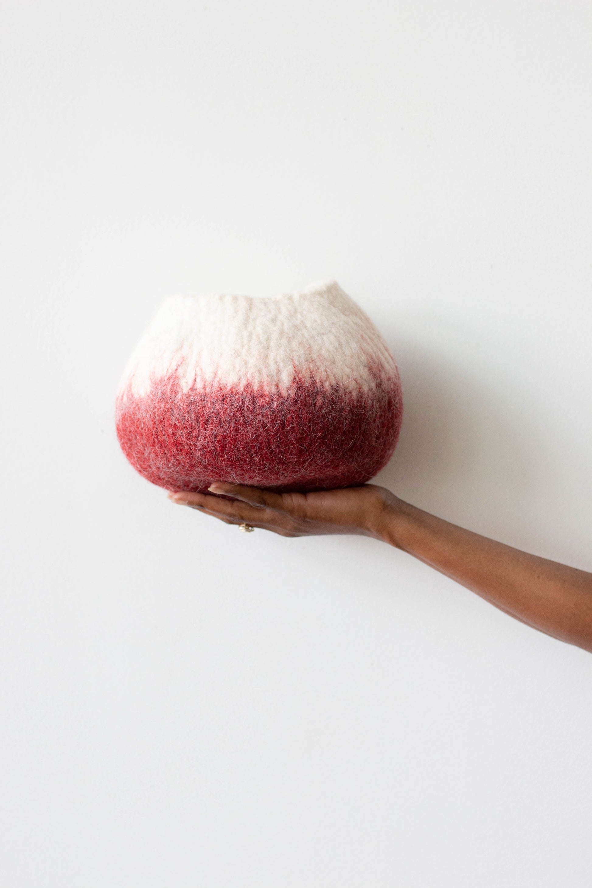 Woman's hand holding white and deep red ombre wool decorative basket against a white background