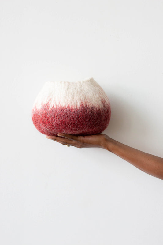 Woman's hand holding white and deep red ombre wool decorative basket against a white background