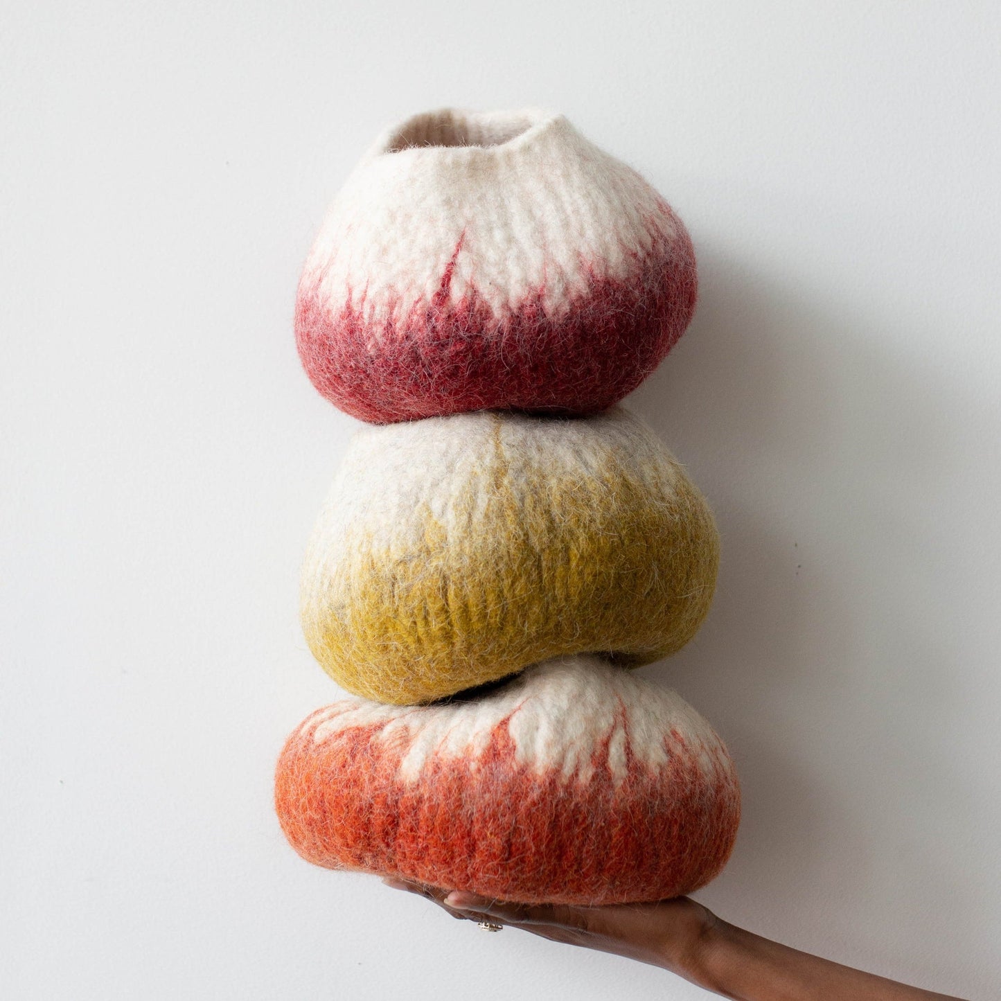 Woman's hand holding a stack of colorful ombre wool decorative baskets against a white background
