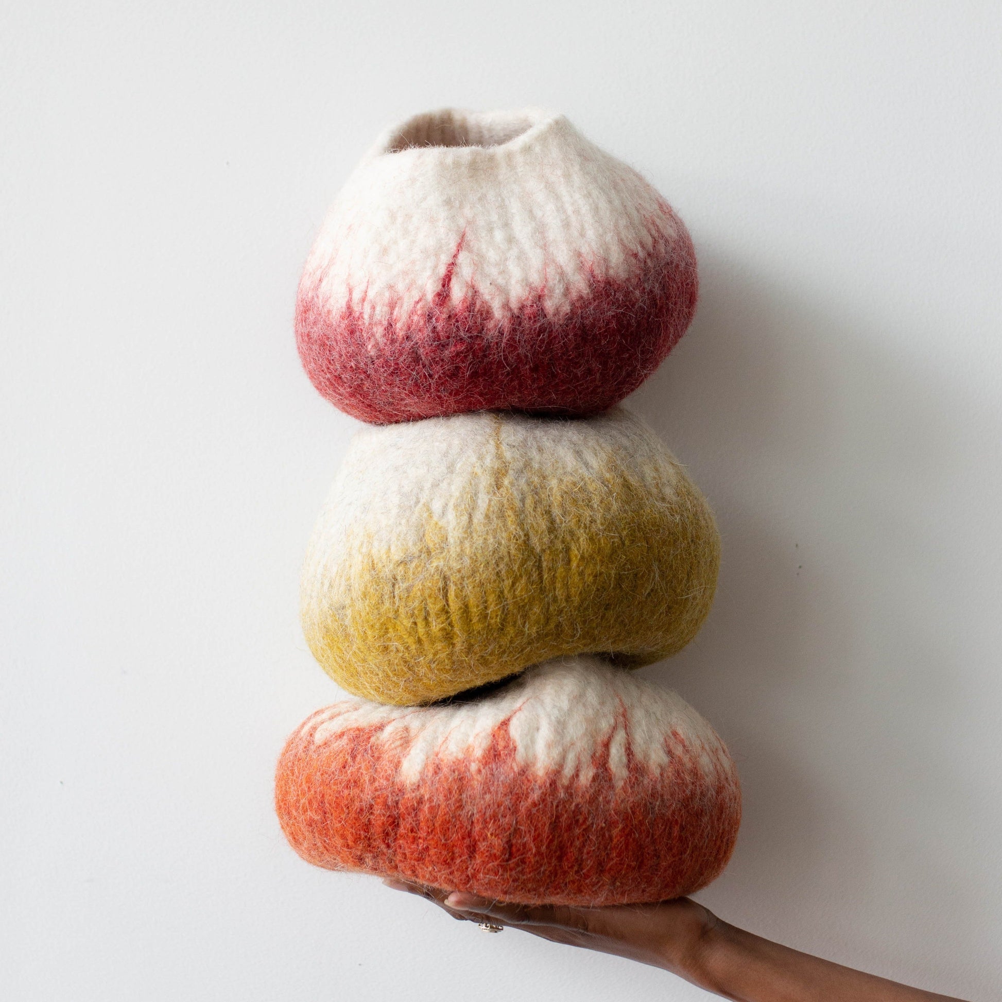 Woman's hand holding a stack of colorful ombre wool decorative baskets against a white background