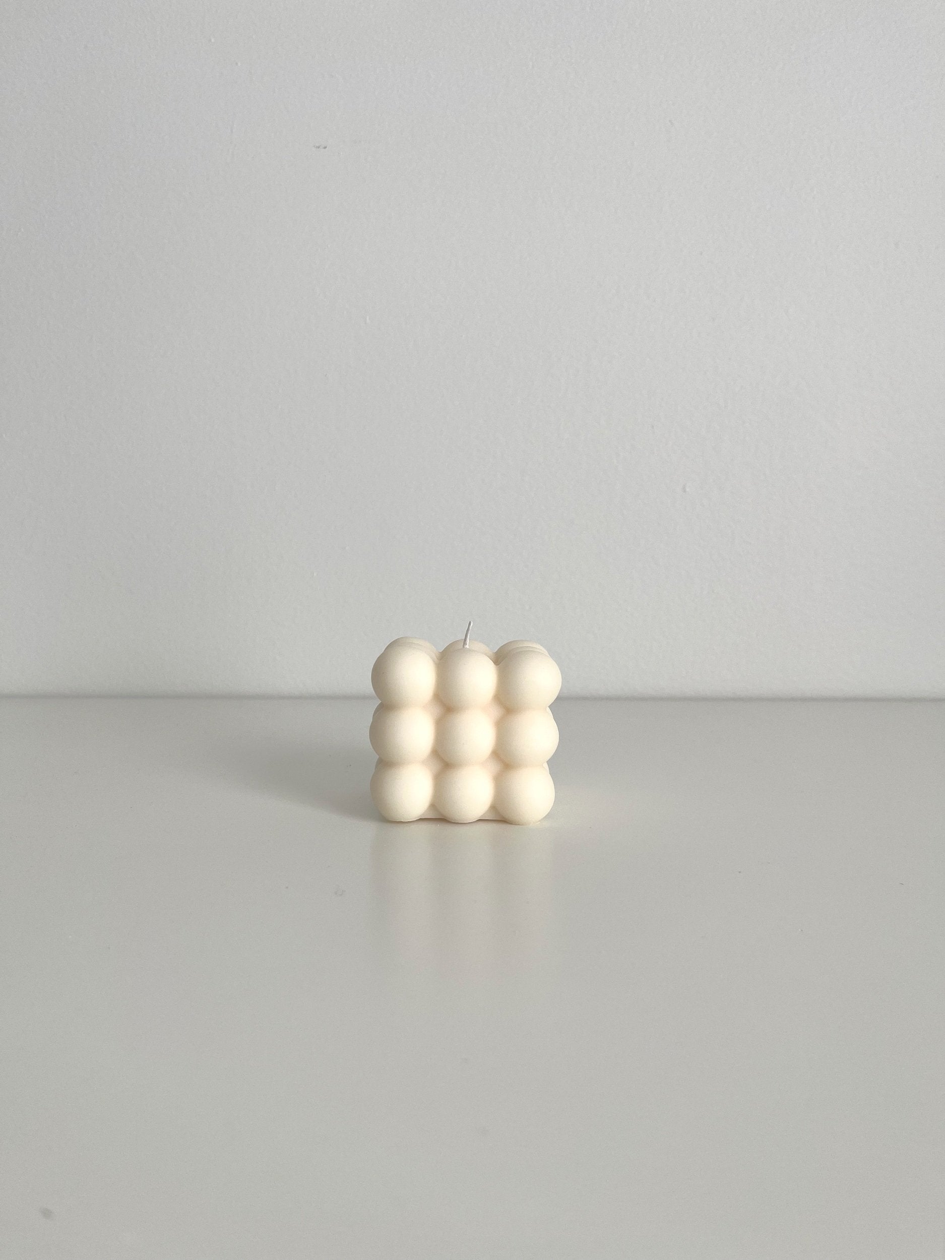 The front view of an ivory bubble cube candle shown sitting on a white surface with a soft gray background