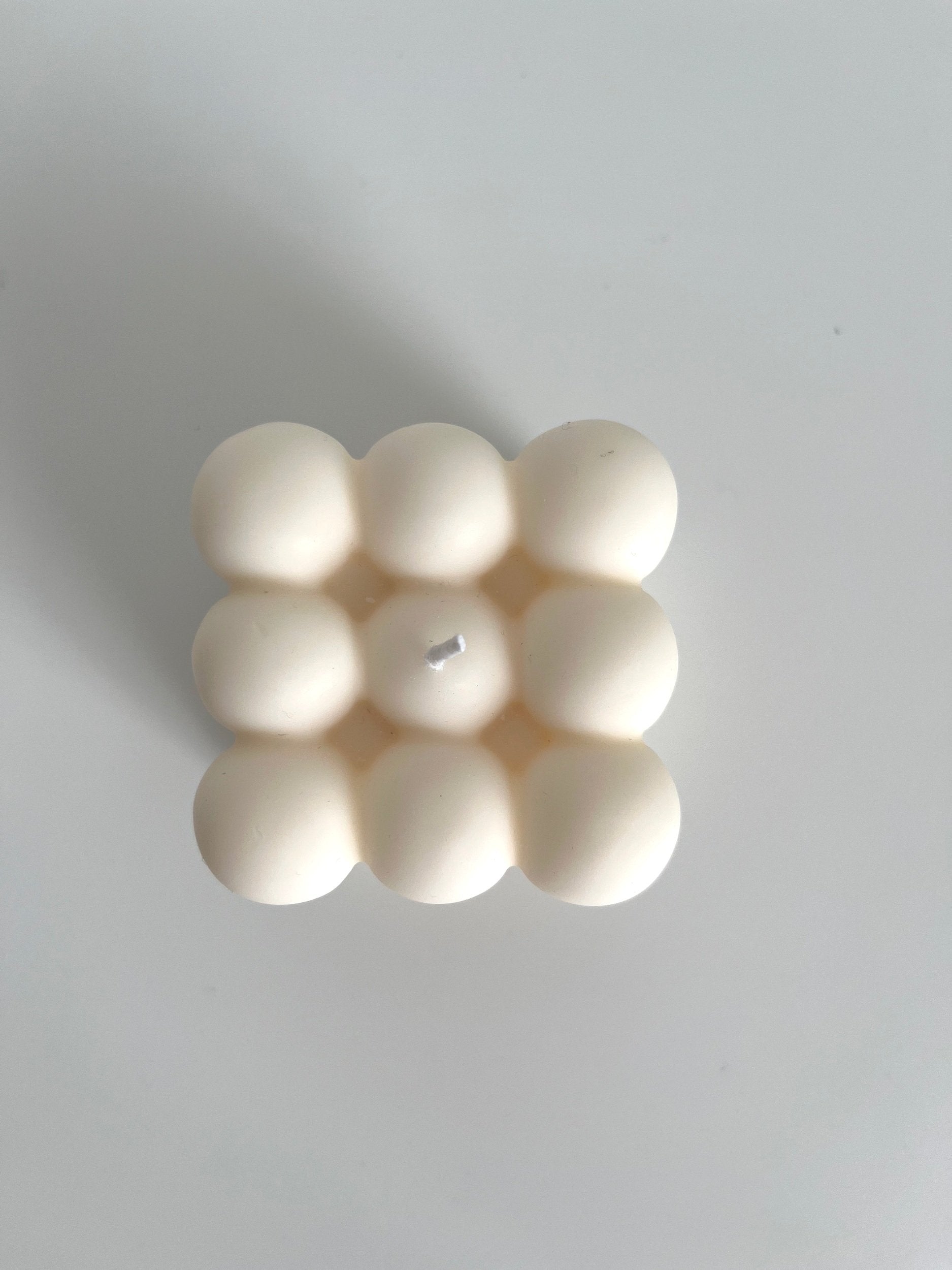 The top view of an ivory bubble cube candle shown sitting on a white surface 