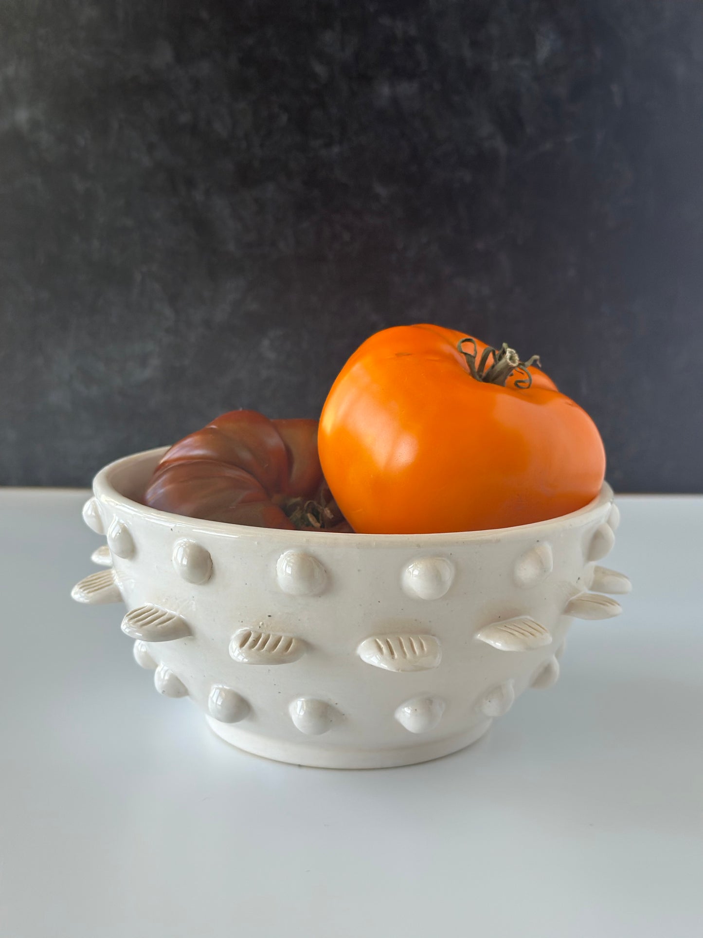 Decorative white bowl with textured surface holding orange and red tomatoes against a dark background