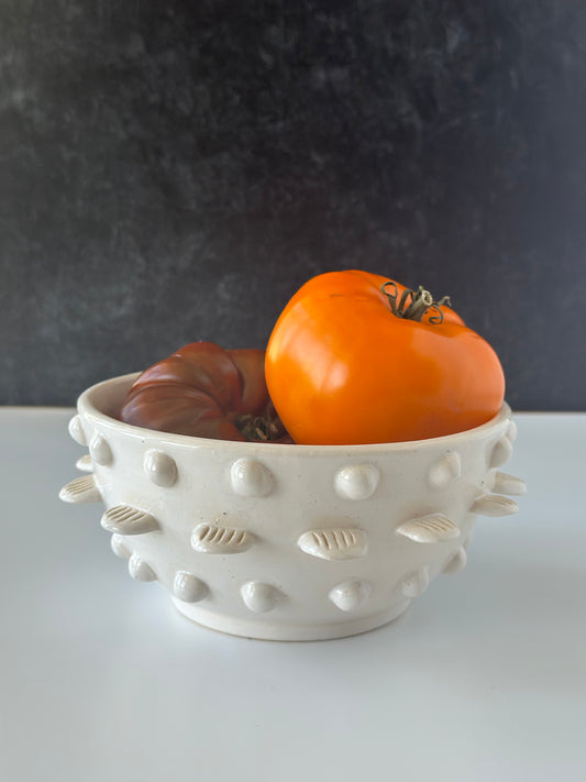 Decorative white bowl with textured surface holding orange and red tomatoes against a dark background