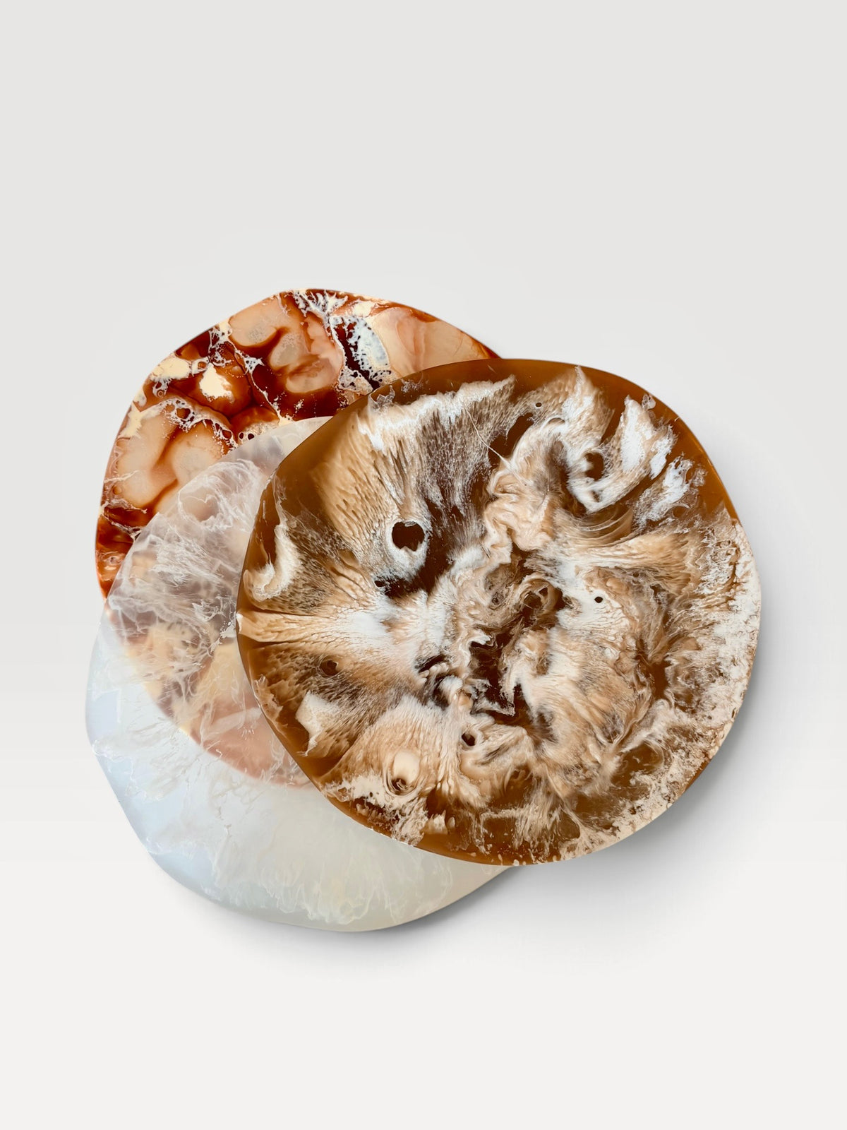 Three round marbled resin platters with  in brown, beige, white, and amber tones, arranged overlapping on a light gray background.