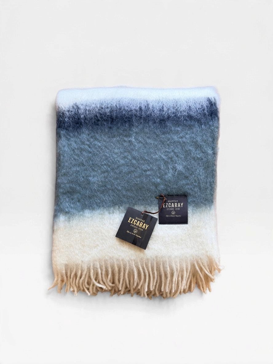 Mantas Ezcaray fringed mohair throw blanket in ivory, light gray and charcoal sitting folded on a white background