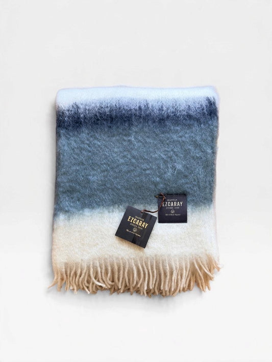 Mantas Ezcaray fringed mohair throw blanket in ivory, light gray and charcoal sitting folded on a white background